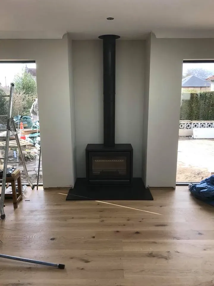 Freestanding stove with exposed flue in a white chimney breast by Agnew Chimney Engineering Glasgow