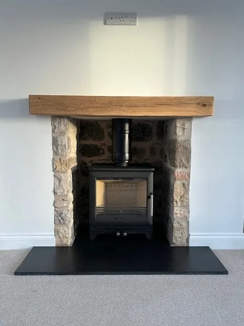 Stove in a natural stone surround with oak beam by Agnew Chimney Engineering Glasgow