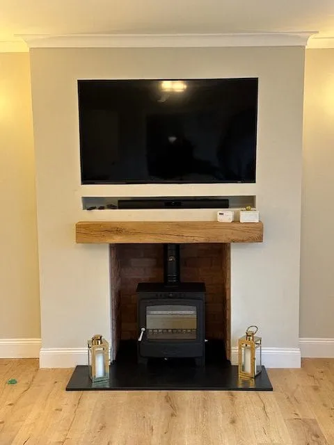 Stove under an oak beam below a wall mounted TV by Agnew Chimney Engineering Glasgow